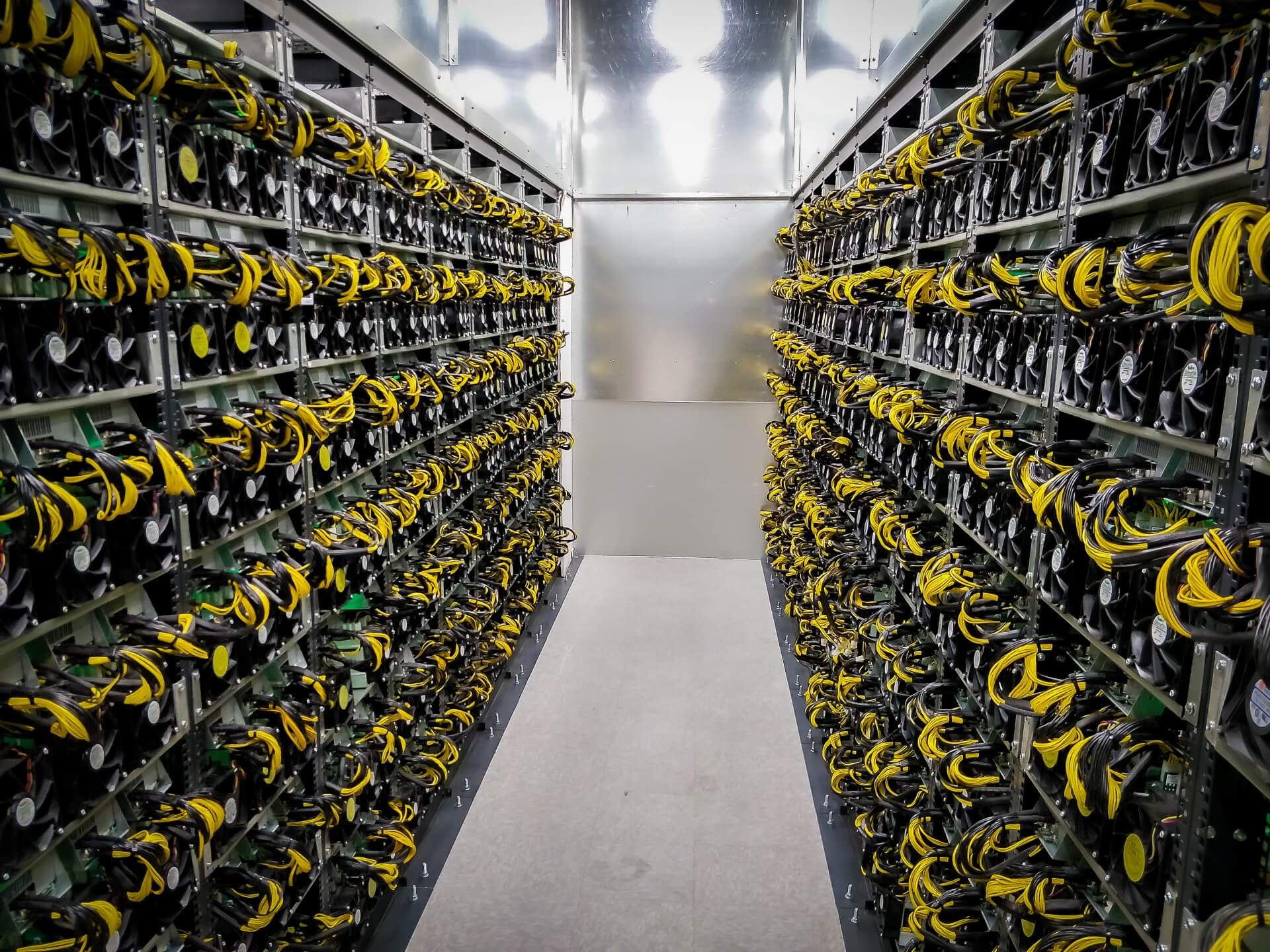 Rows of ASIC mining machines inside a large industrial Bitcoin mining facility, showing how mining moved from ordinary home computers in 2009 to warehouse-scale operations